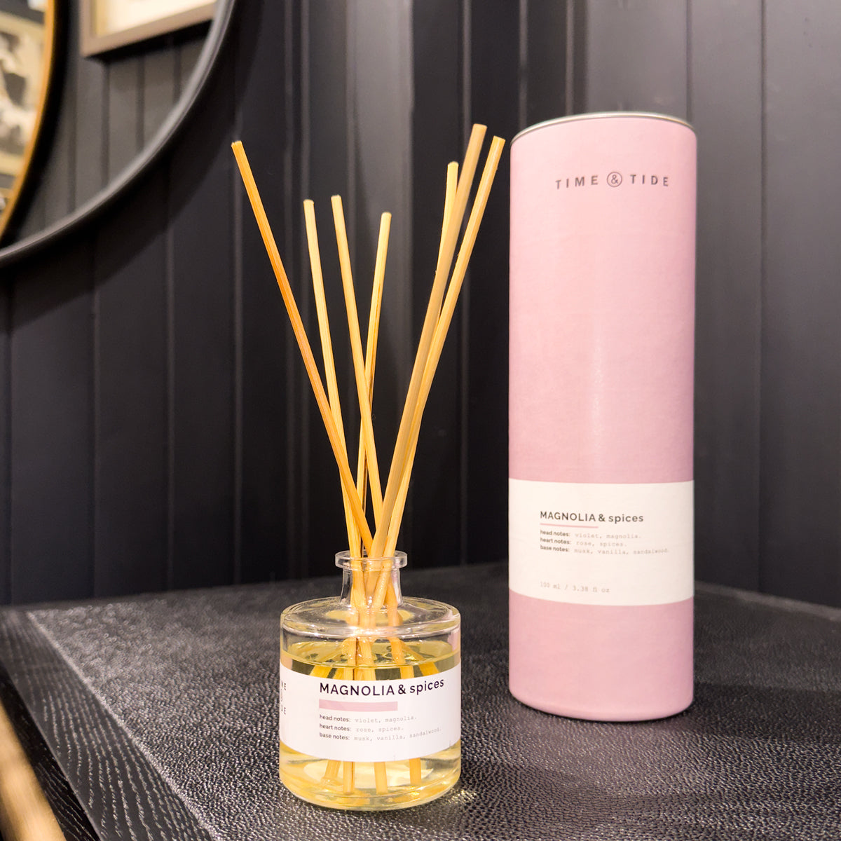 Diffuser with reeds and pink cylindrical container on a dark surface