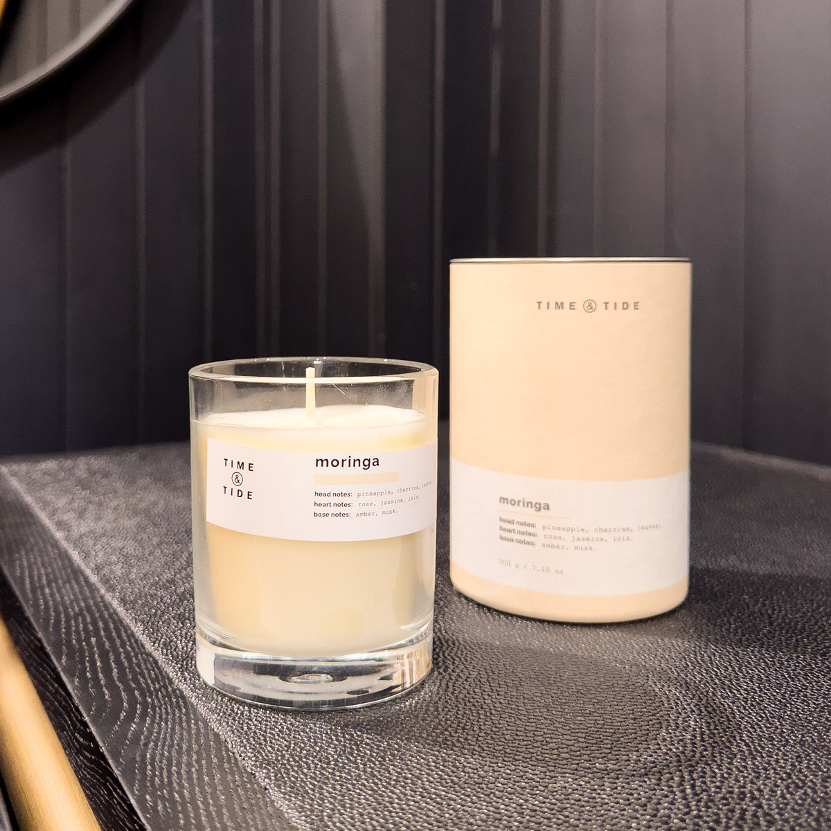 Candle and its packaging labeled 'Time & Tide' on a textured surface.