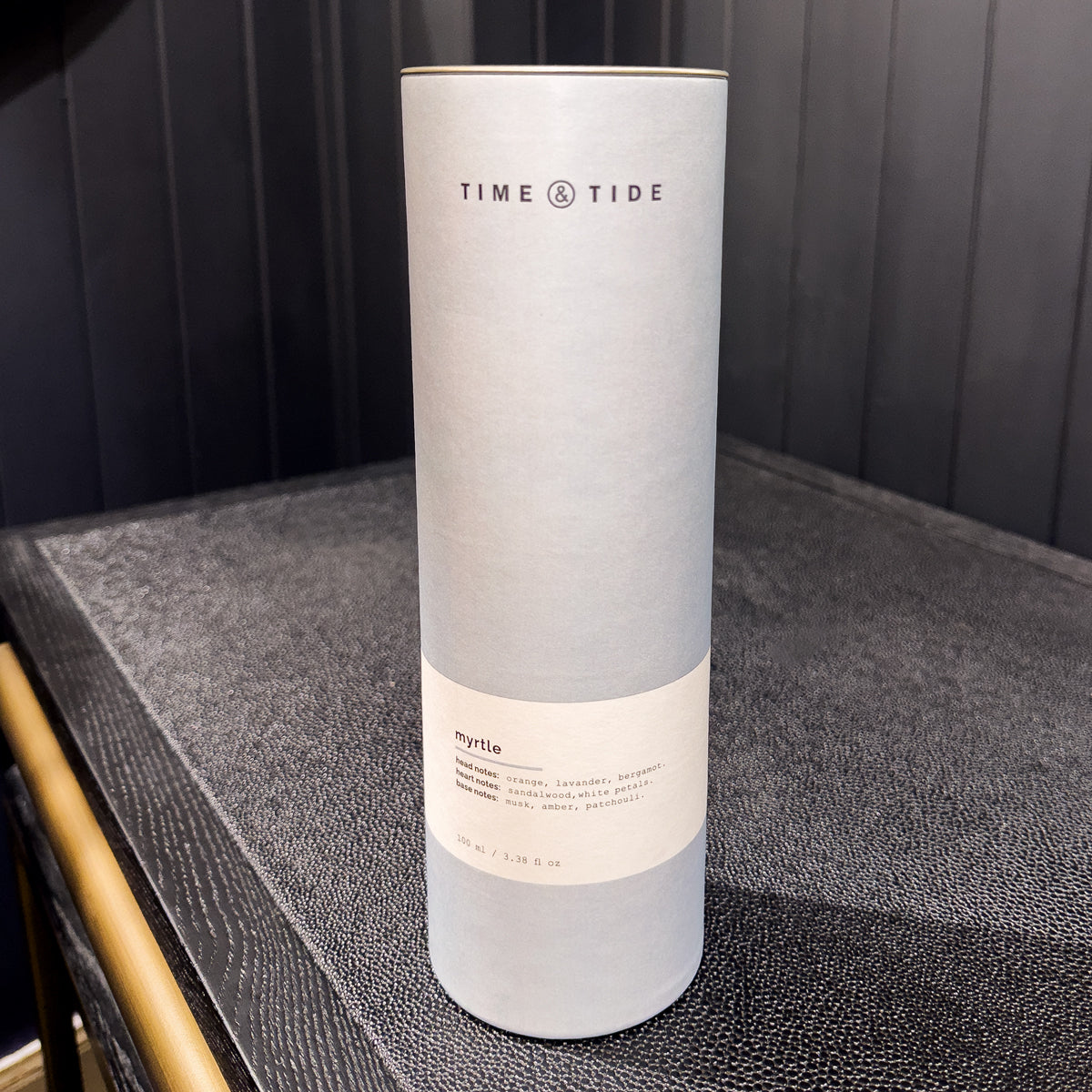 Bottle of 'Time & Tide' home fragrance product on a textured surface with a dark background