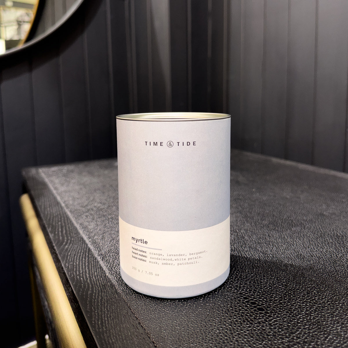 Candle labeled 'Time & Tide' on a dark surface with a blurred background