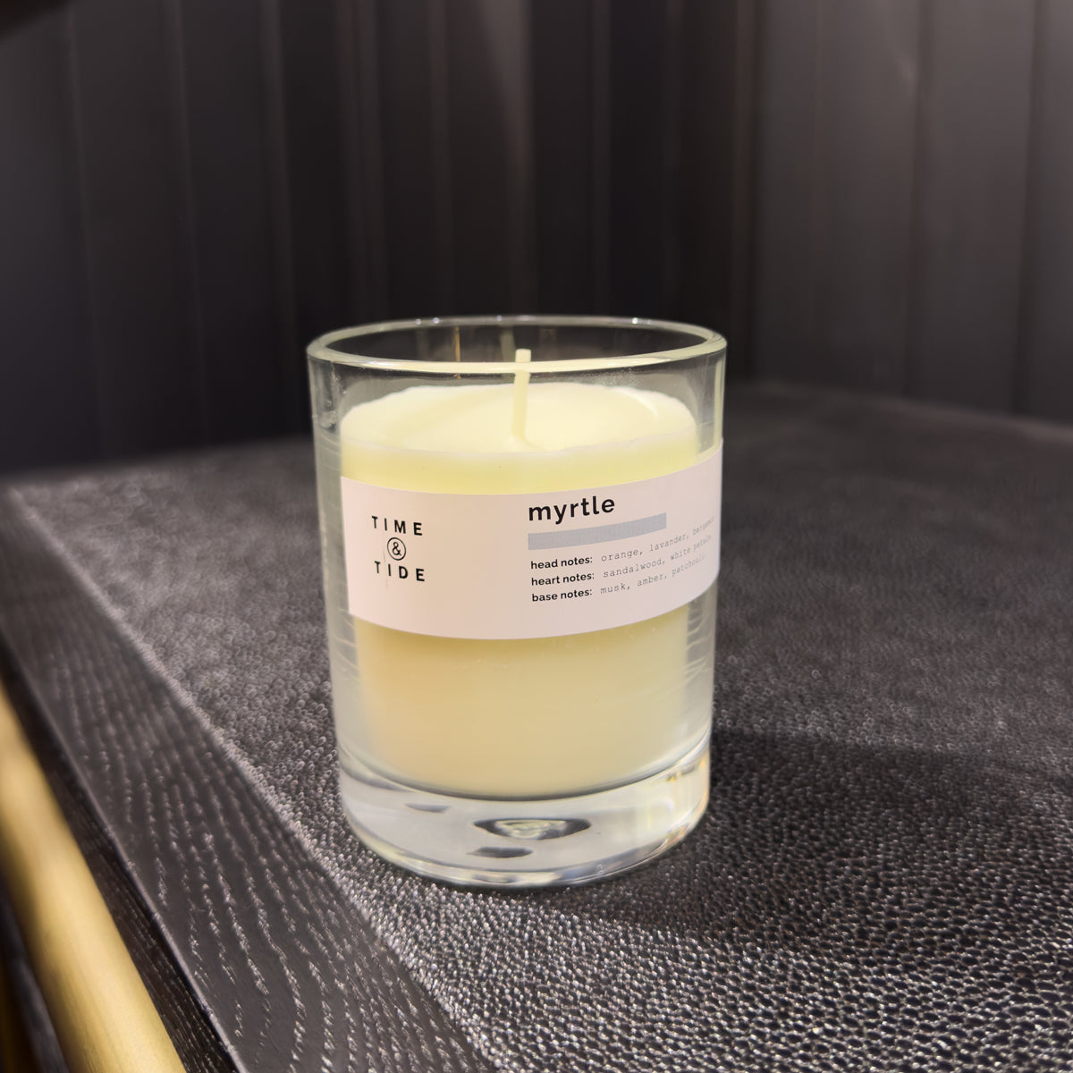 Candle labeled 'myrtle' by 'Time & Tide' on a textured surface with a dark background