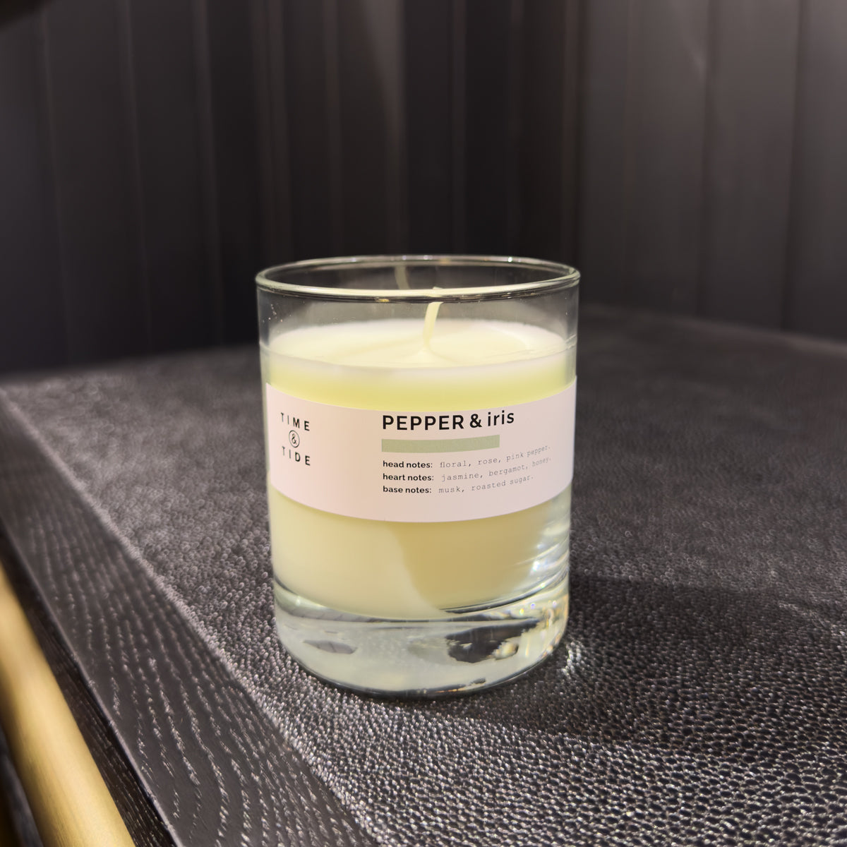 Candle labeled 'Pepper & Iris' on a dark surface