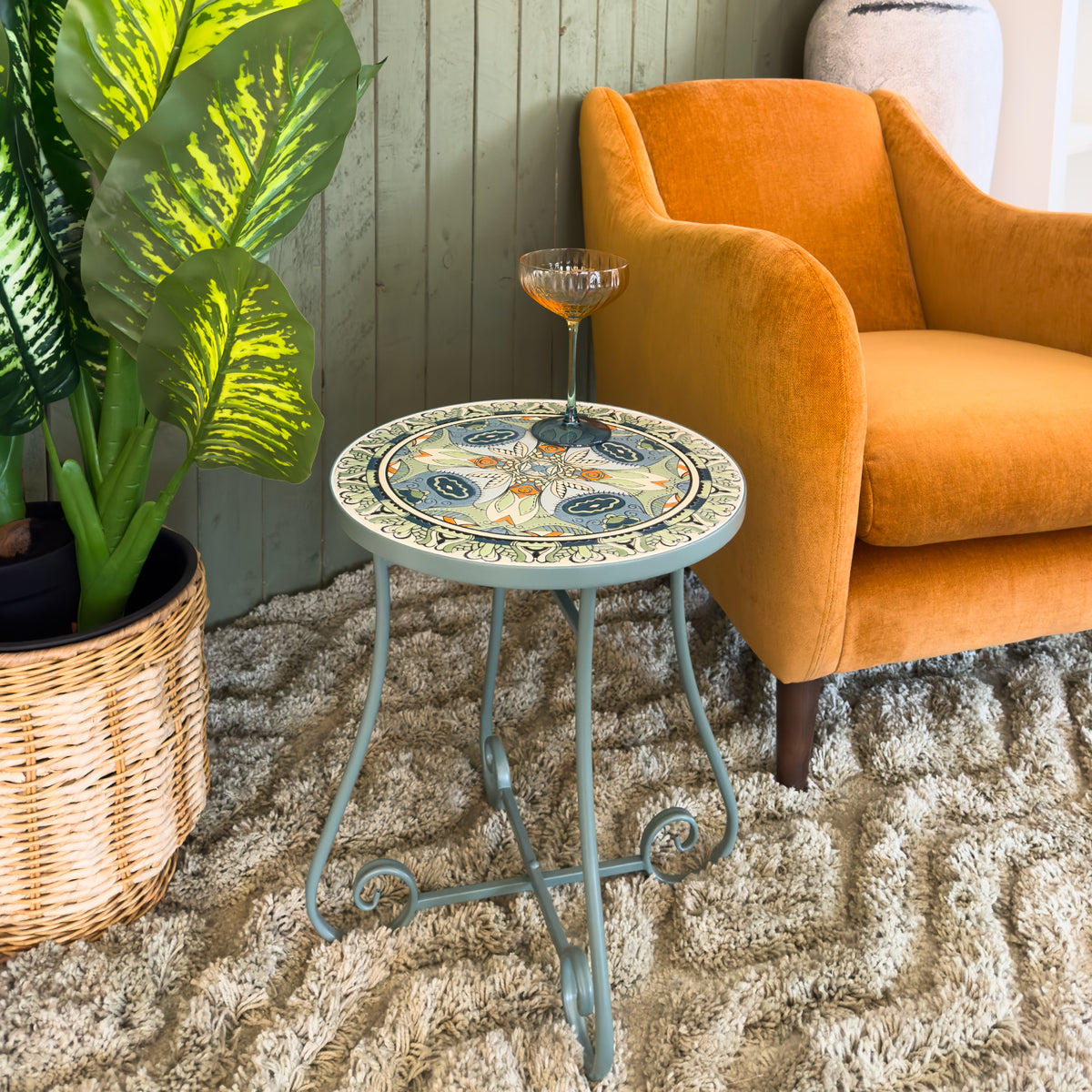 Teal mosaic side table with a colouful mosaic design next to an orange armchair and potted plant.