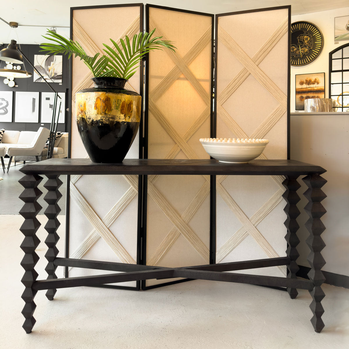 Decorative console table with a vase and plant in front of a folding screen