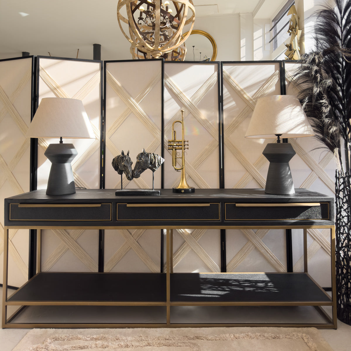 A black and gold console table with two black minimalist lamps, a double horse sculpture and a gold trumpet on top.