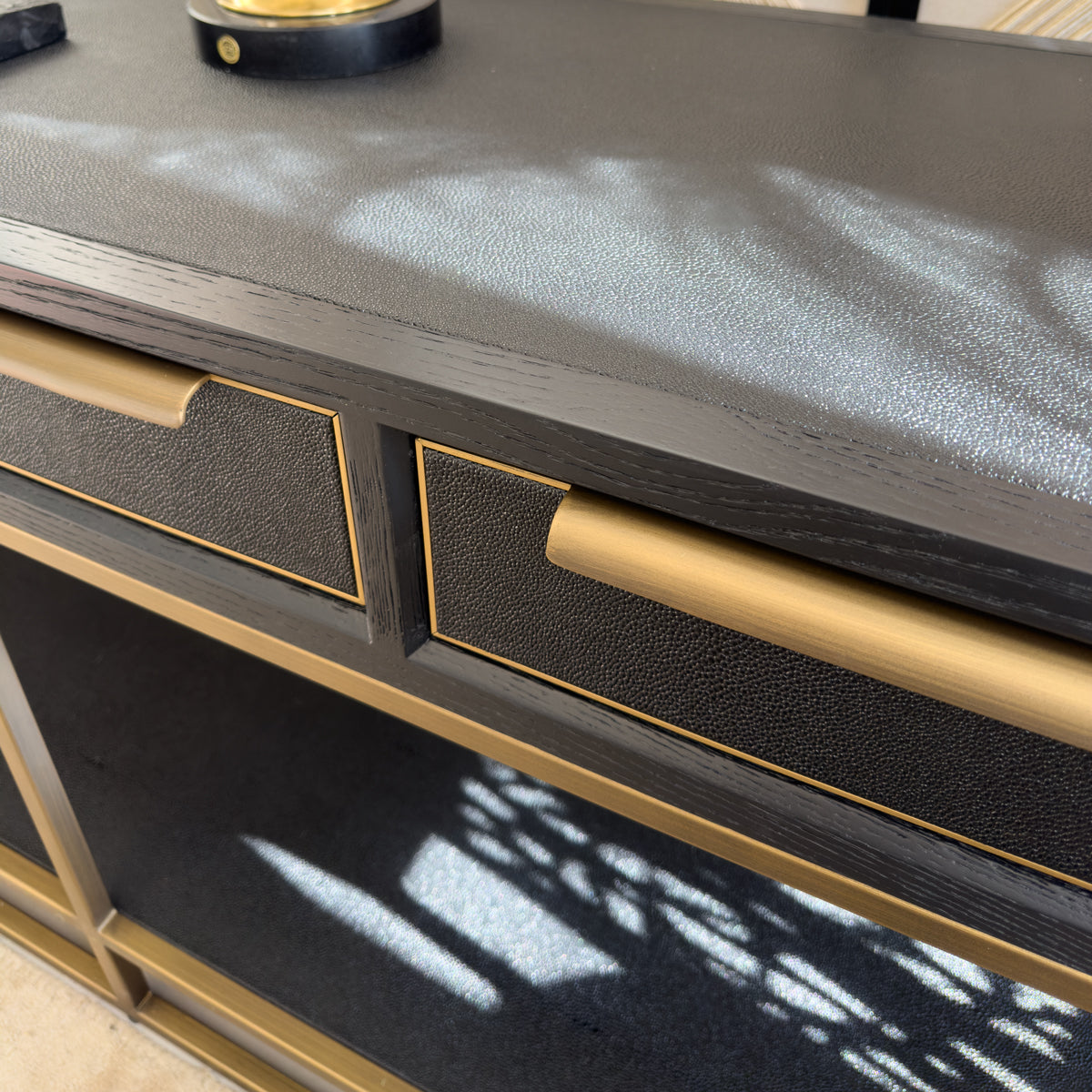 A close up of a black and gold console table with narrow golden handles.