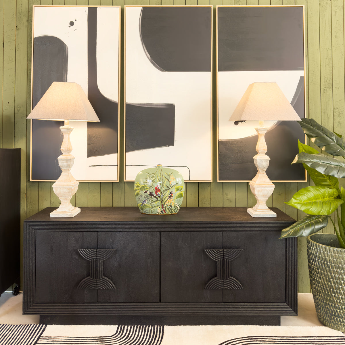 Dark wooden console table with two lamps and a decorative vase against a green wall with abstract art.