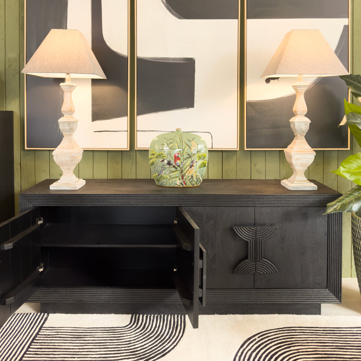 Black cabinet with open door, decorative items, and lamps against a green wall.
