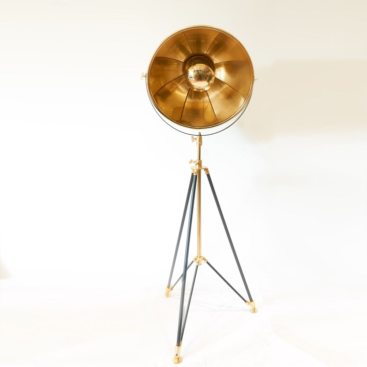 A gold studio floor lamp with tripod base against a white backdrop