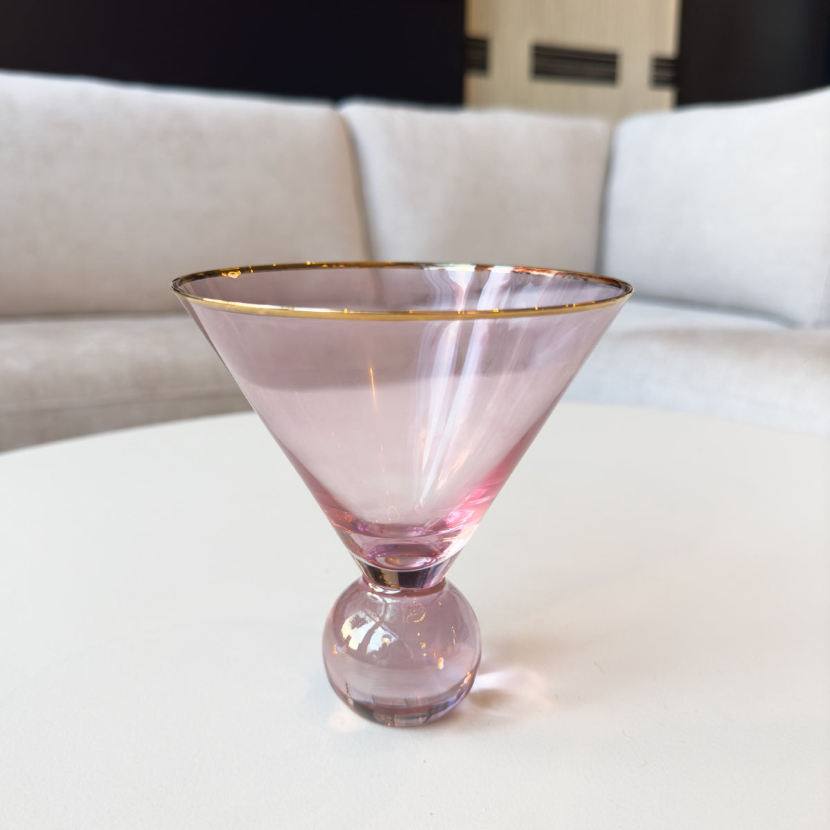 Pink ball base martini glass with gold rim on a white surface
