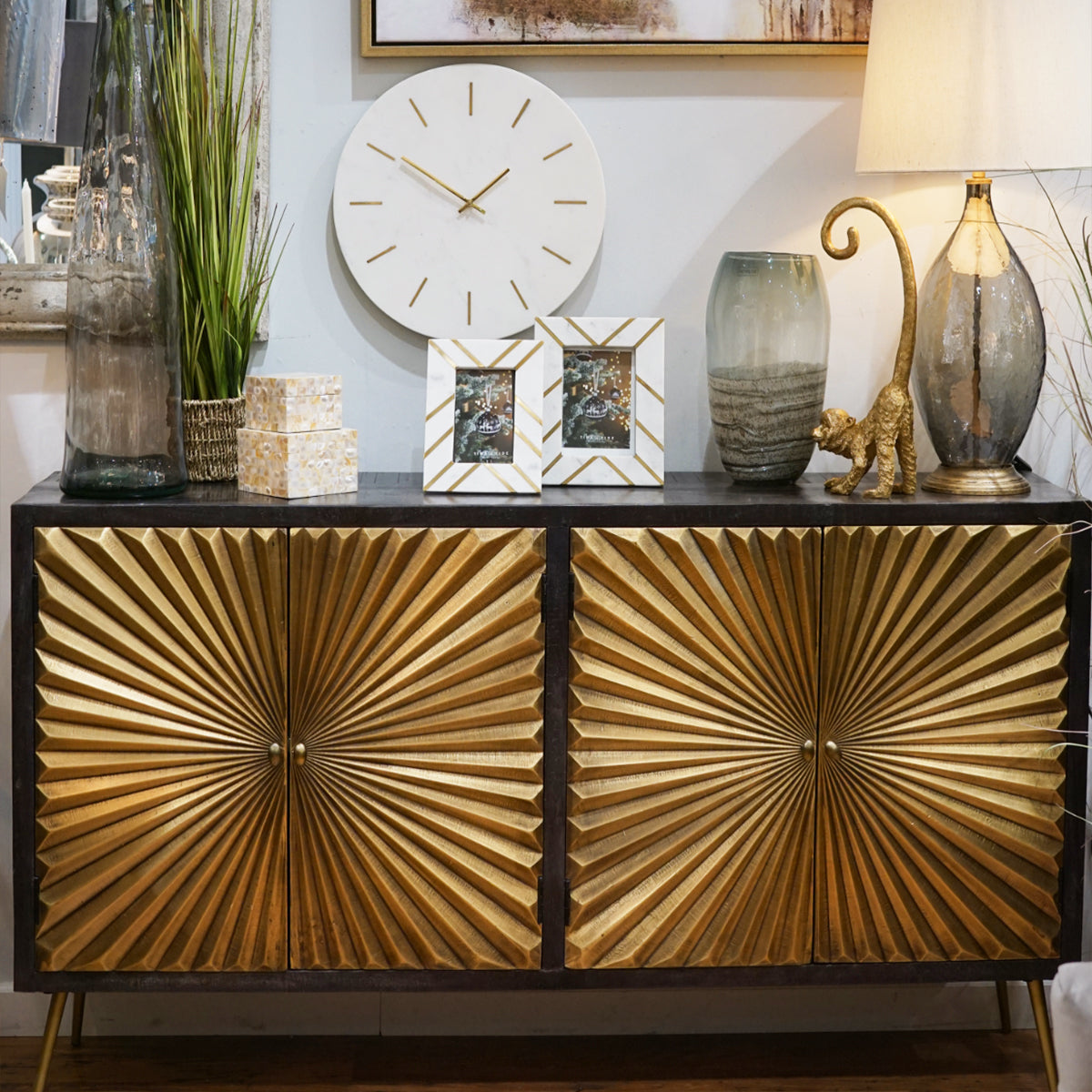 Gold starburst cabinet with gold sunburst design, clock, and lamps.