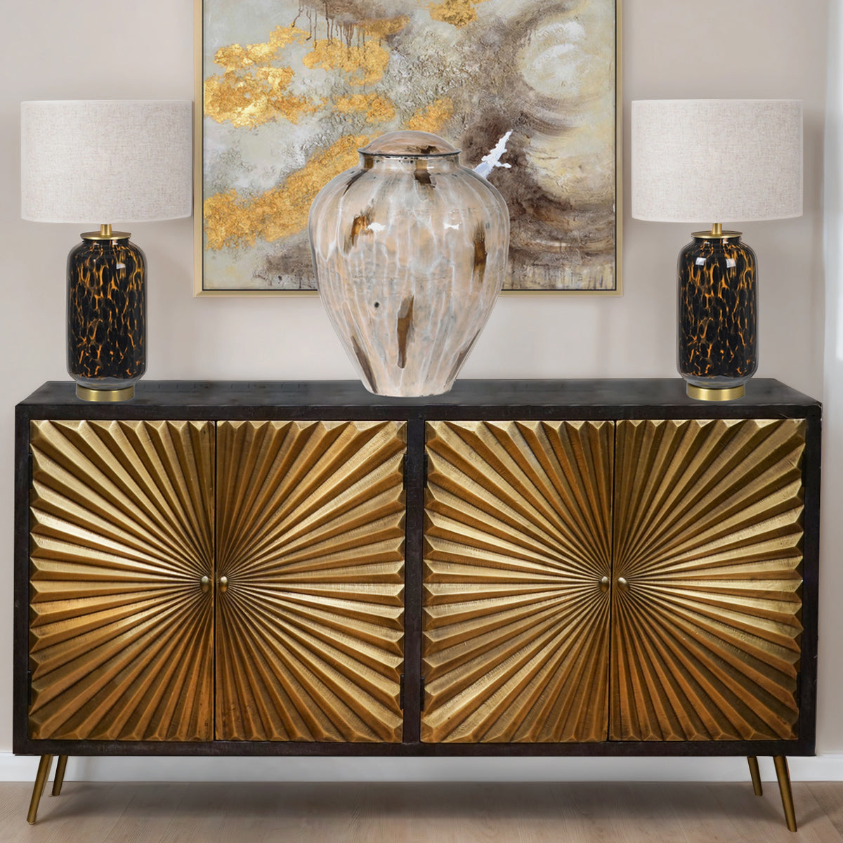 Decorative sideboard with gold sunburst design, with two tortoiseshell table lamps and a abstract painting.