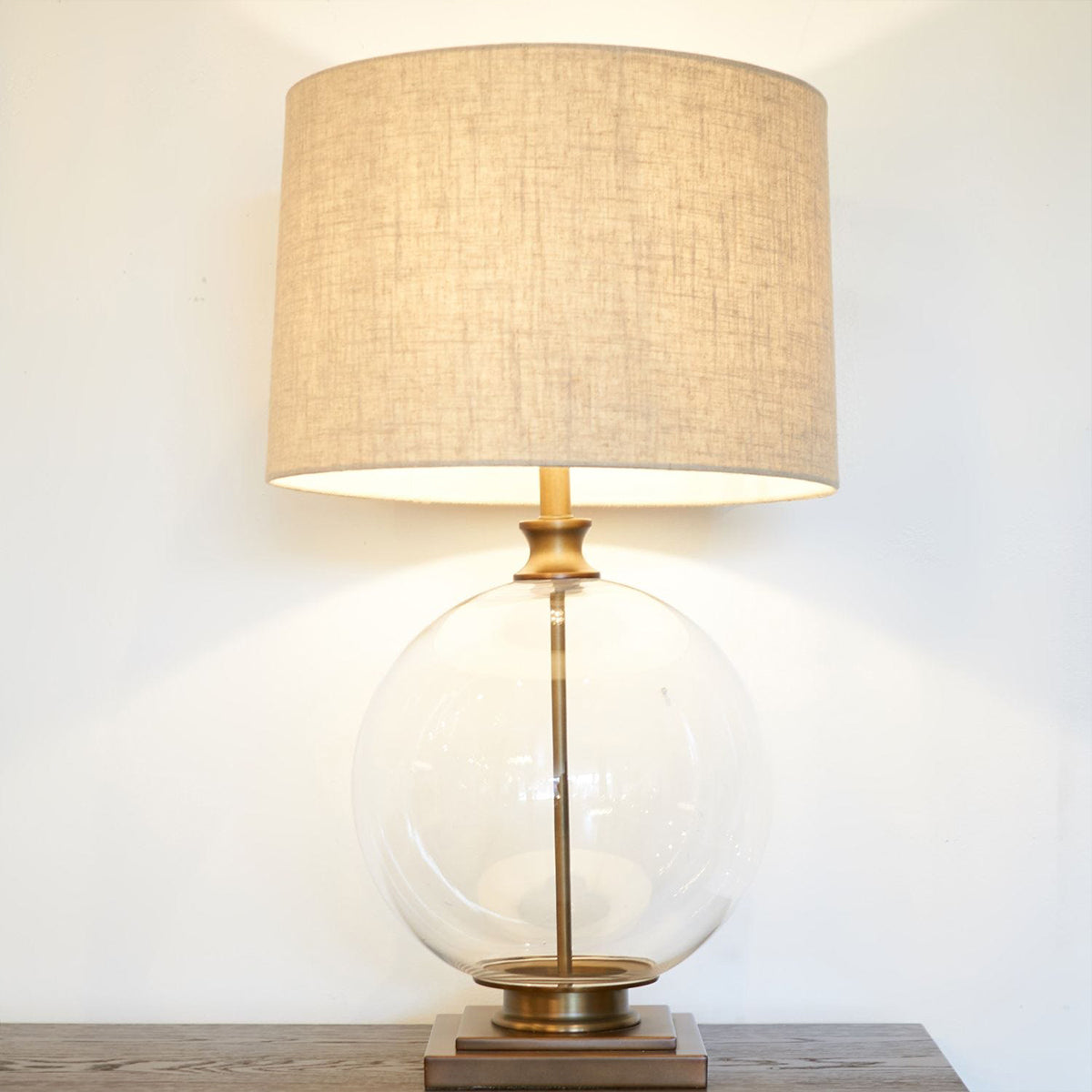 A round glass lamp with a neutral linen shade and bronze accents on the neck and base.