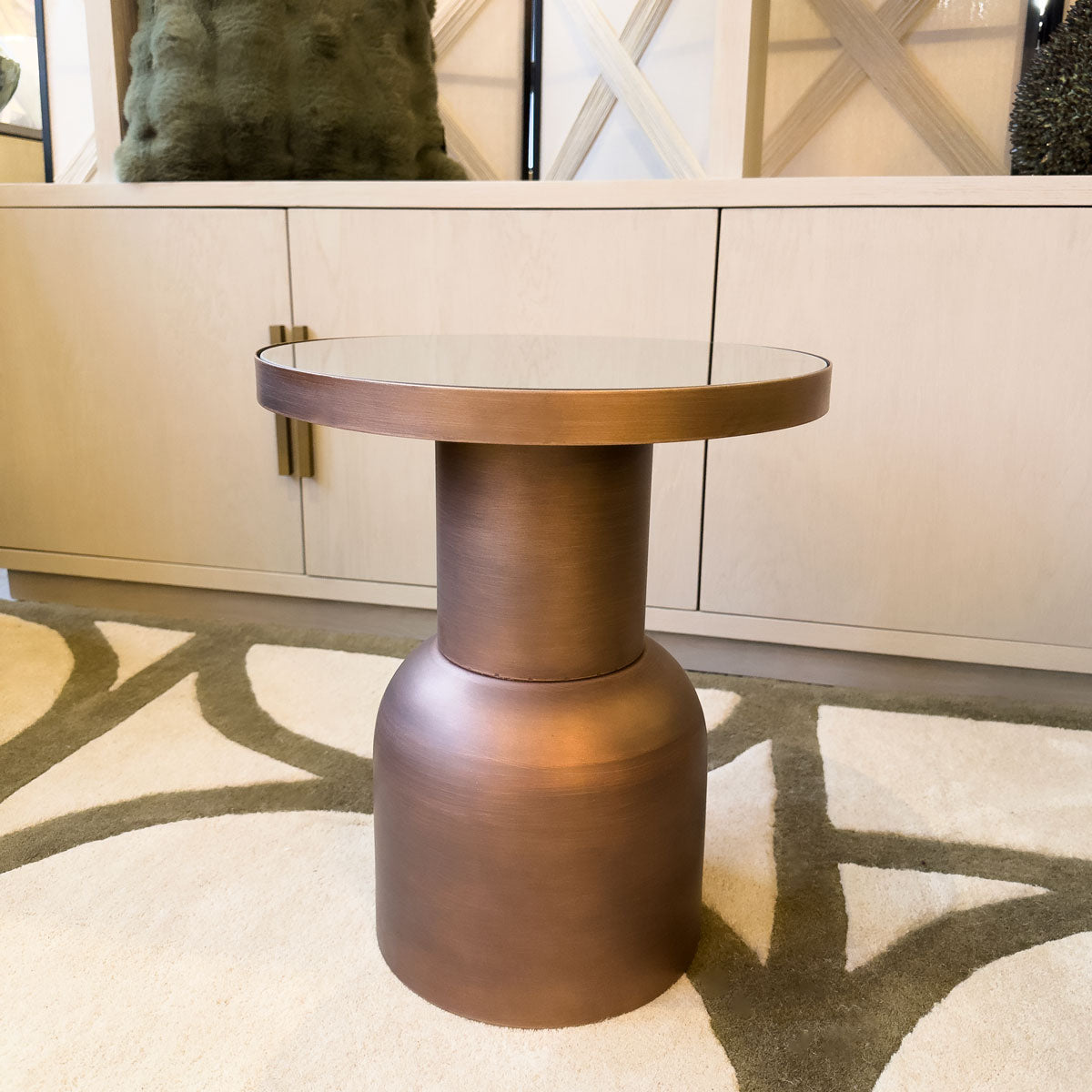 Bronze side table in a room with a patterned rug and neutral shelving unit.