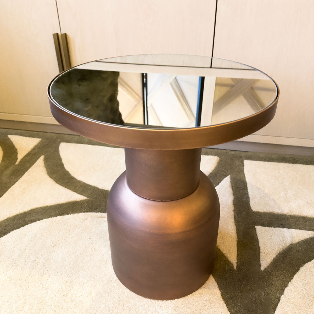 Round glass-top side table with bronze base on a patterned rug