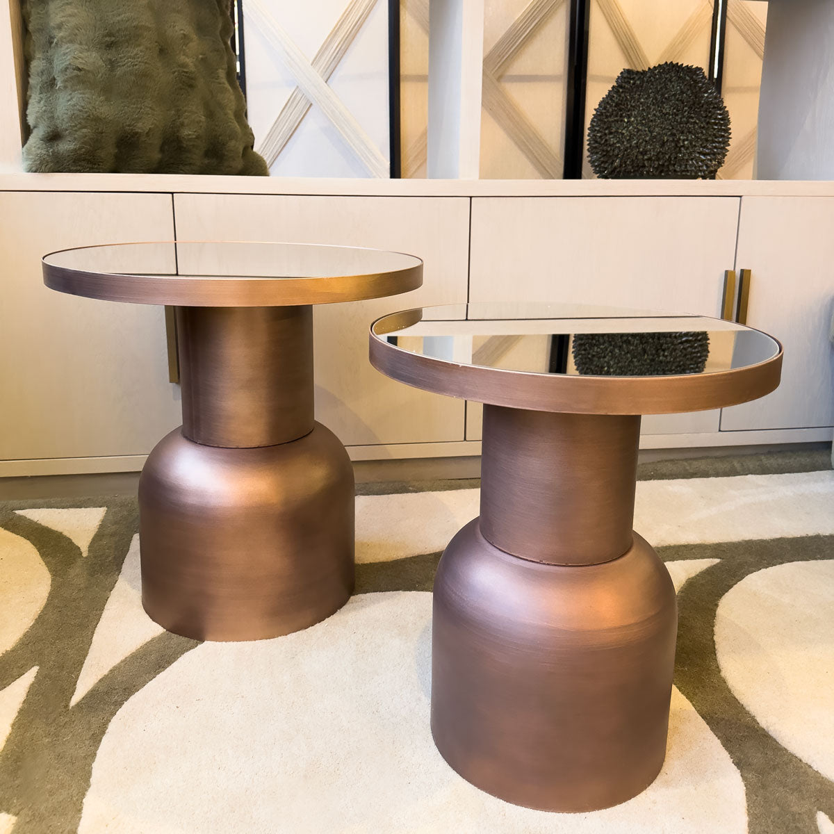 Two bronze-colored side tables on a patterned rug with a neutral wall in the background.