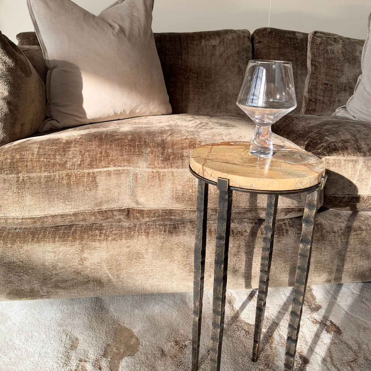 Small brown marble round side table with a glass aside a textured sofa