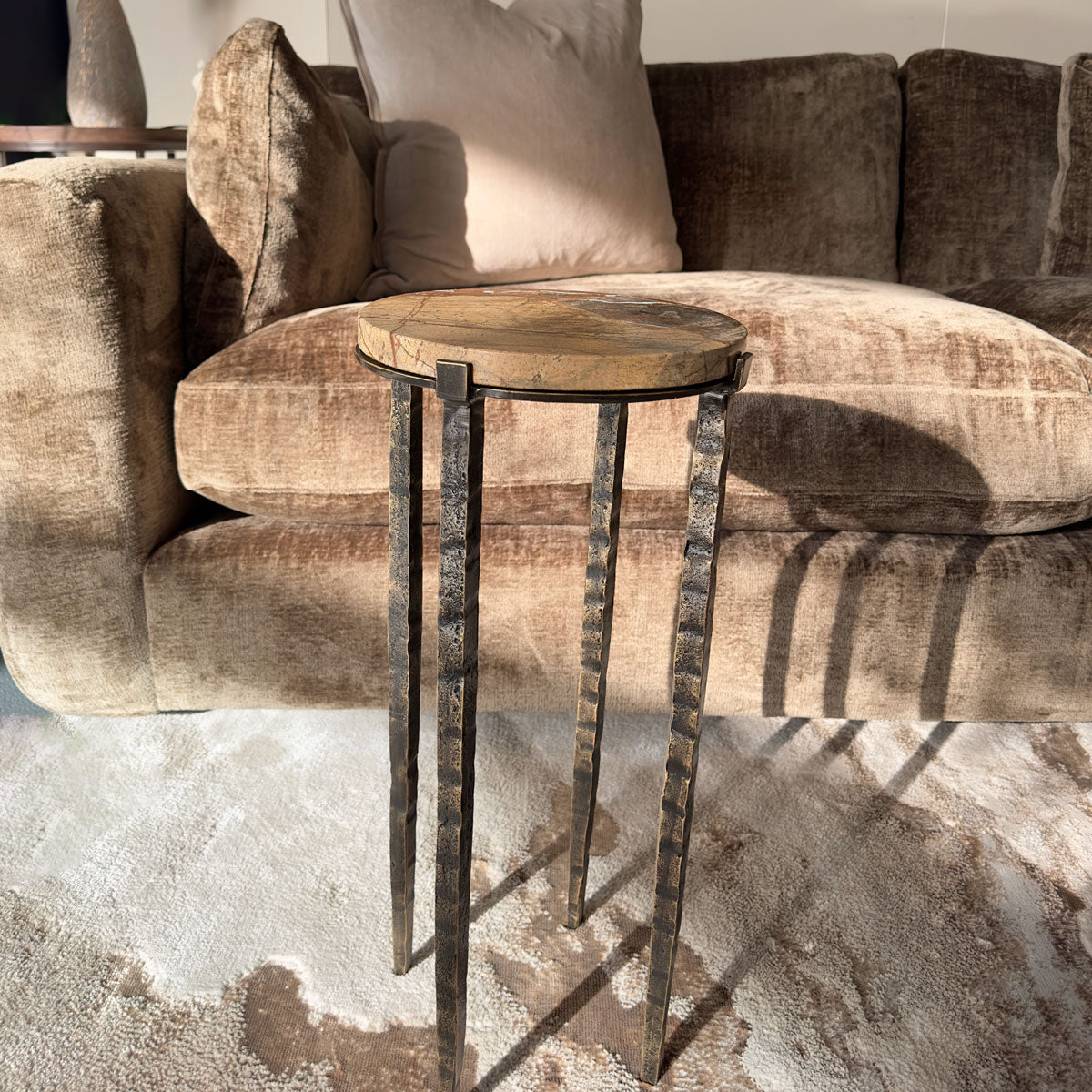 Marble side table with hammered metal legs in front of a brown sofa.
