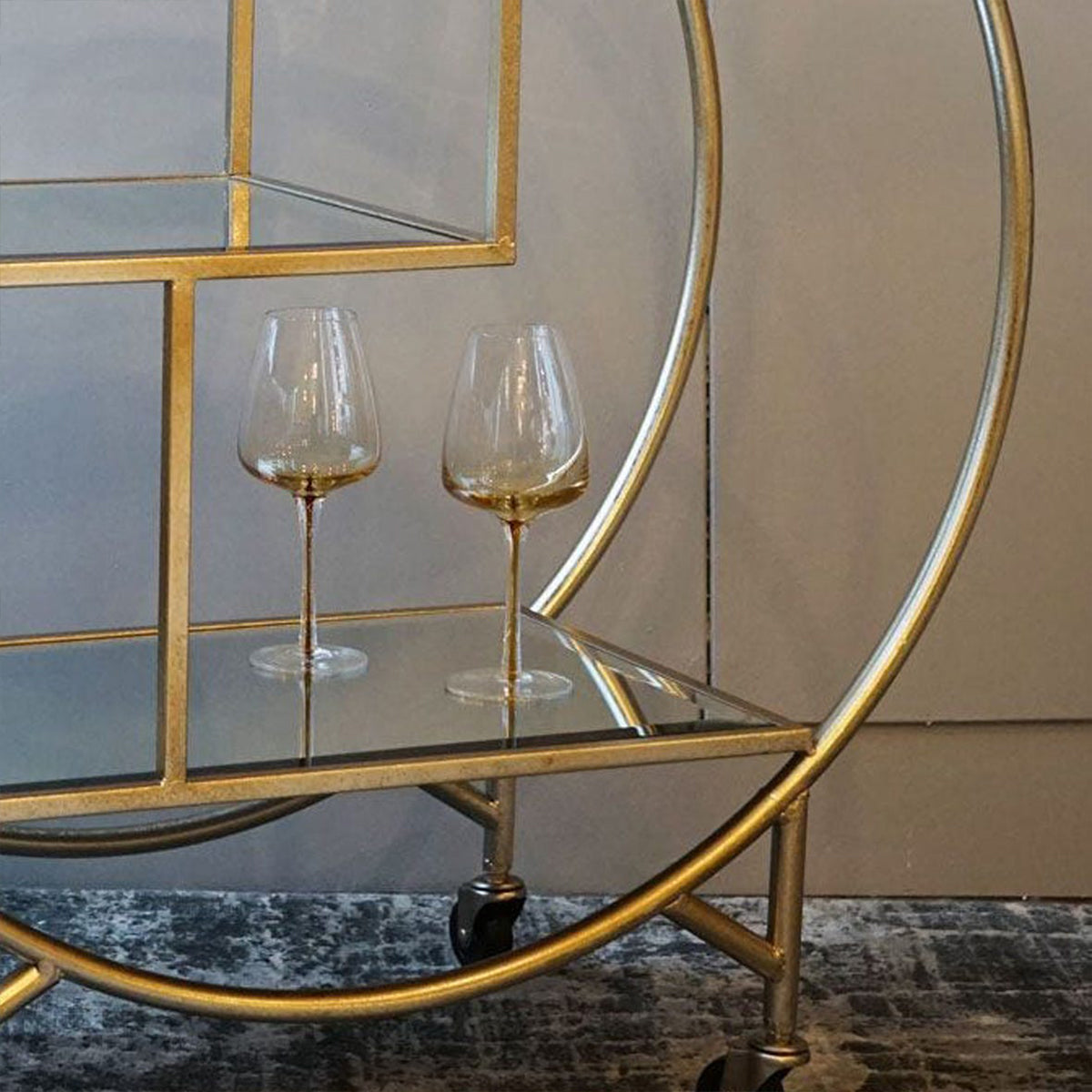 Gold bar cart with two wine glasses on a reflective surface.
