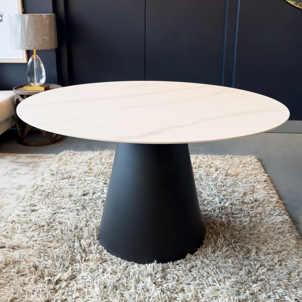 Round dining table with white marble top and black base on a textured rug.