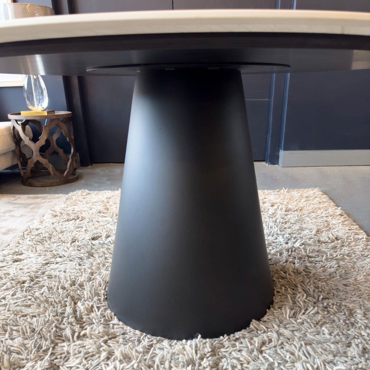 Black cylindrical table leg on a textured rug with a blurred background