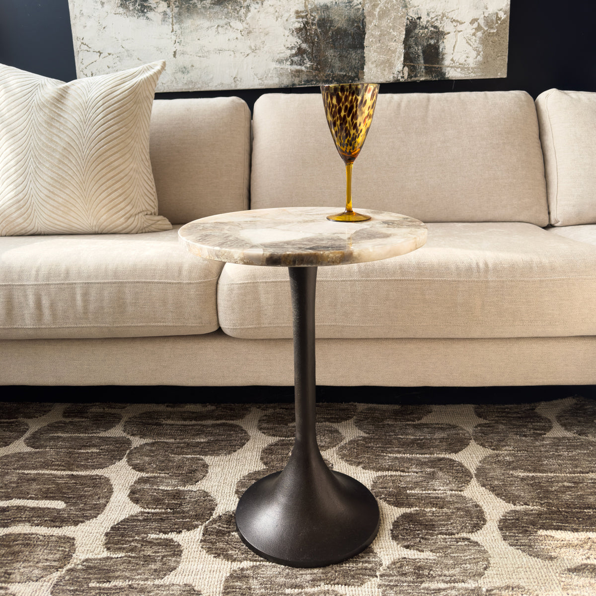 Round marble table with a black base in front of a beige sofa.