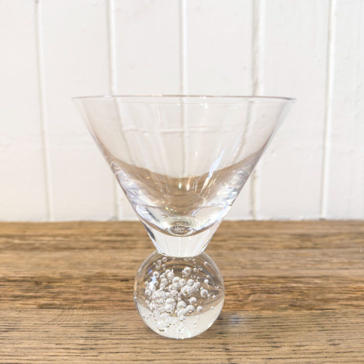Clear glass with bubble design on a wooden surface and white panelled wall background