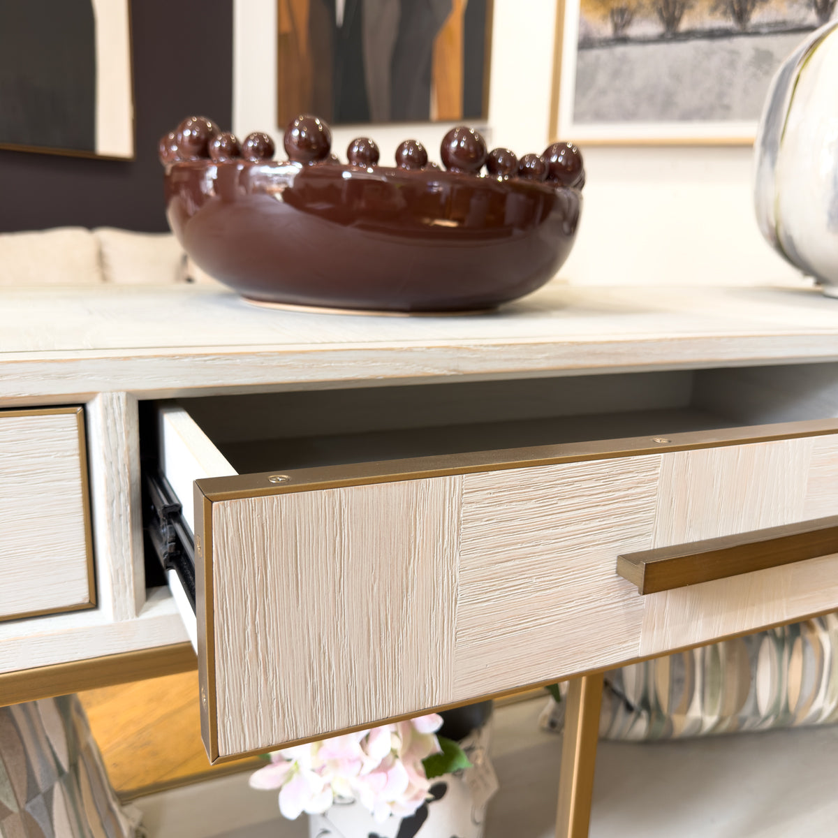 A close-up of a parquet console table drawer with a light cream wood grain finish and a gold metal handle.