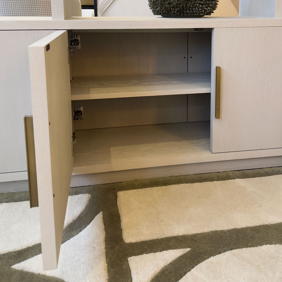 Light wooden shelving unit with open cabinet door on a patterned rug