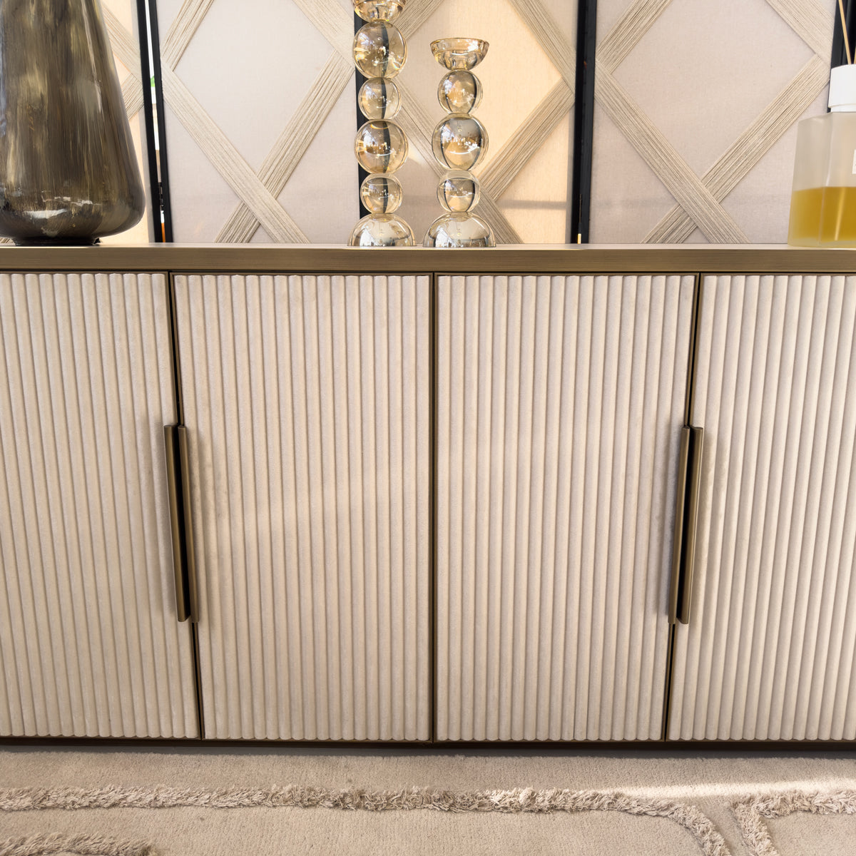 A close up of a cream ridged sideboard with gold handles, with two bubbled glass candleholders on top.