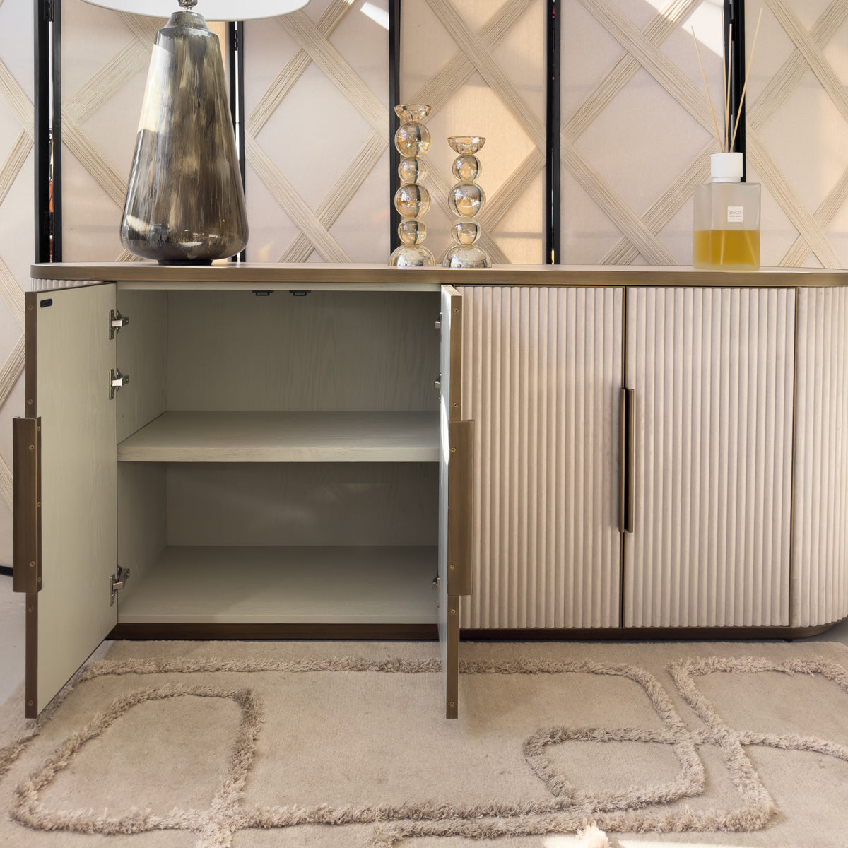 A cream sideboard with gold details, with two doors open revealing an internal storage shelf.