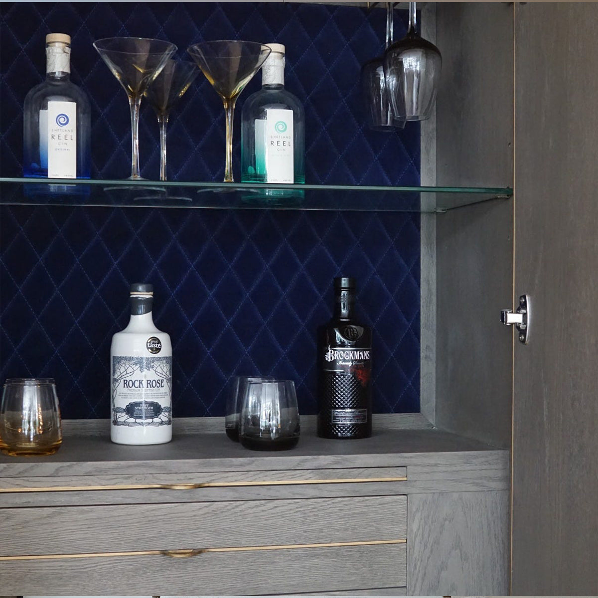 Alcohol bottles and glasses on a bar shelf with a blue velvet lining on the bar cabinet