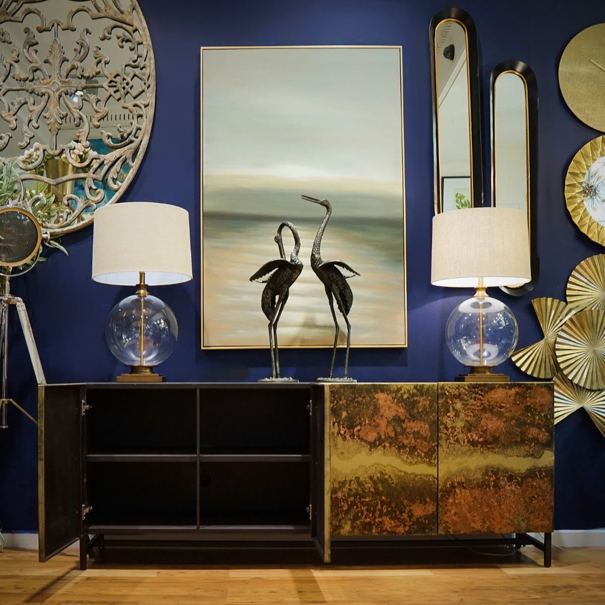 Decorative interior setting with a blue wall, art pieces, lamps, and a cabinet.