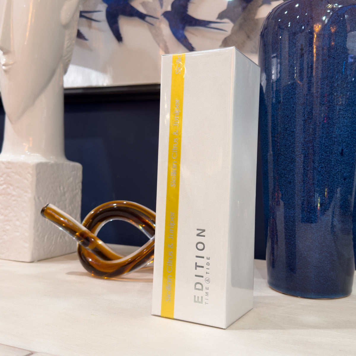 Product packaging with a yellow stripe and 'Edition' branding on a shelf with decorative items.