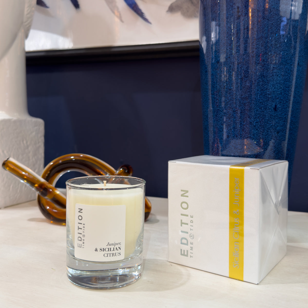 Candle with a box labeled 'Edition' on a surface with decorative items in the background.