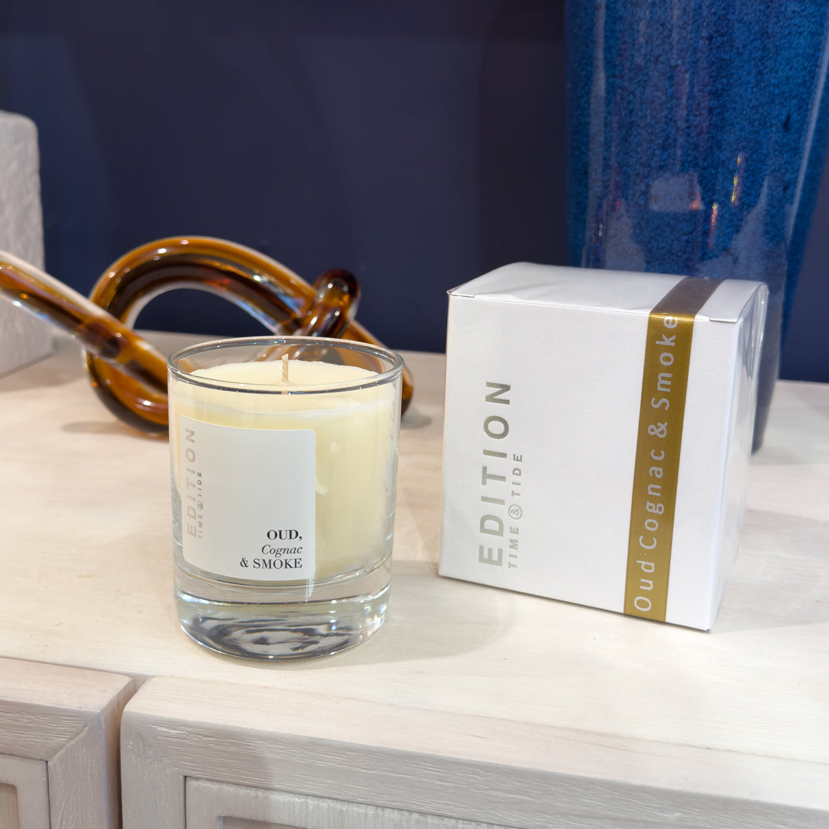 Candle labeled 'Oud Cognac & Smoke' with a matching box on a wooden surface.