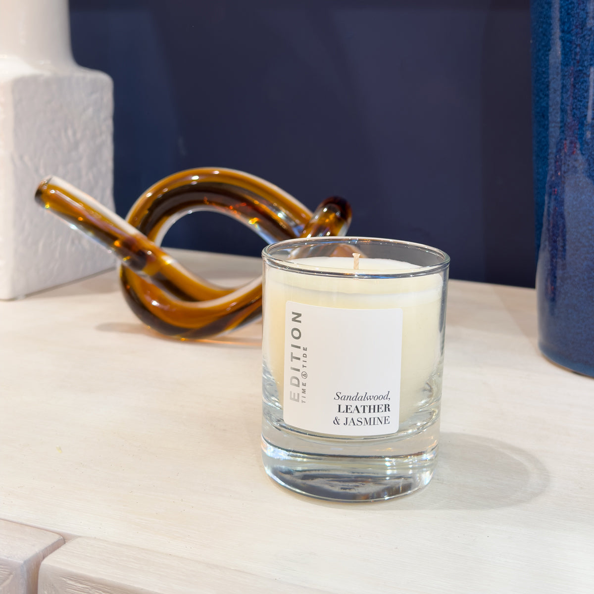 Candle with a label on a surface, with decorative objects in the background