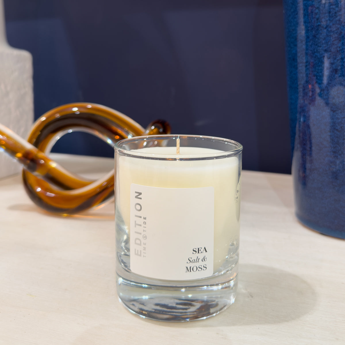 Candle labeled 'Sea Salt & Moss' on a surface with decorative items in the background