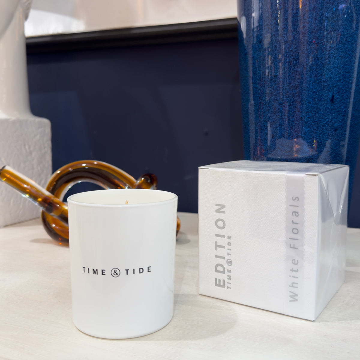 White candle with 'Time & Tide' branding next to a box of 'Edition White Florals' on a surface.