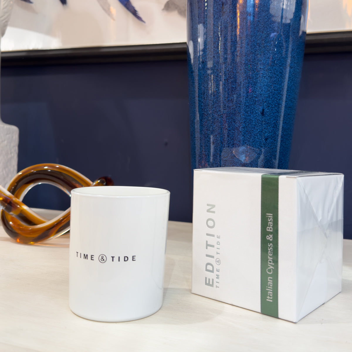 White candle with 'Time & Tide' branding next to a box of 'Edition' candles on a surface.