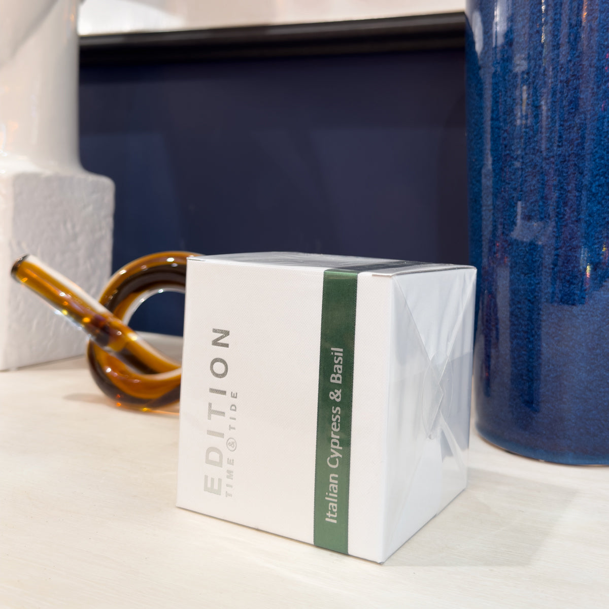 White box with green text labeled 'Edition' on a surface with a blue vase and brown object in the background.