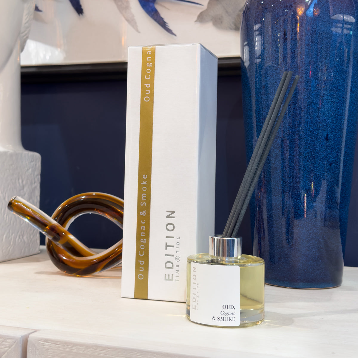 A diffuser bottle with a box labeled 'Oud Cognac & Smoke' on a decorative surface.