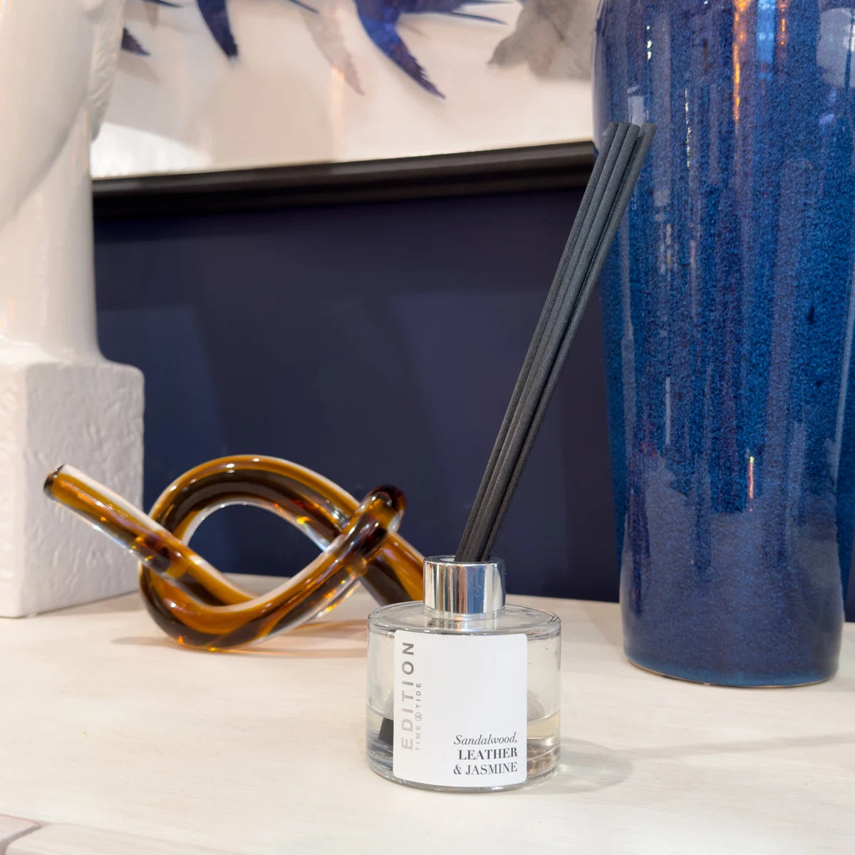Leather scent diffuser bottle with reeds on a surface next to decorative items