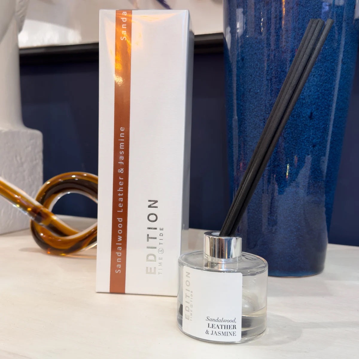 Sandalwood Leather & Jasmine diffuser with packaging and a blue vase in the background
