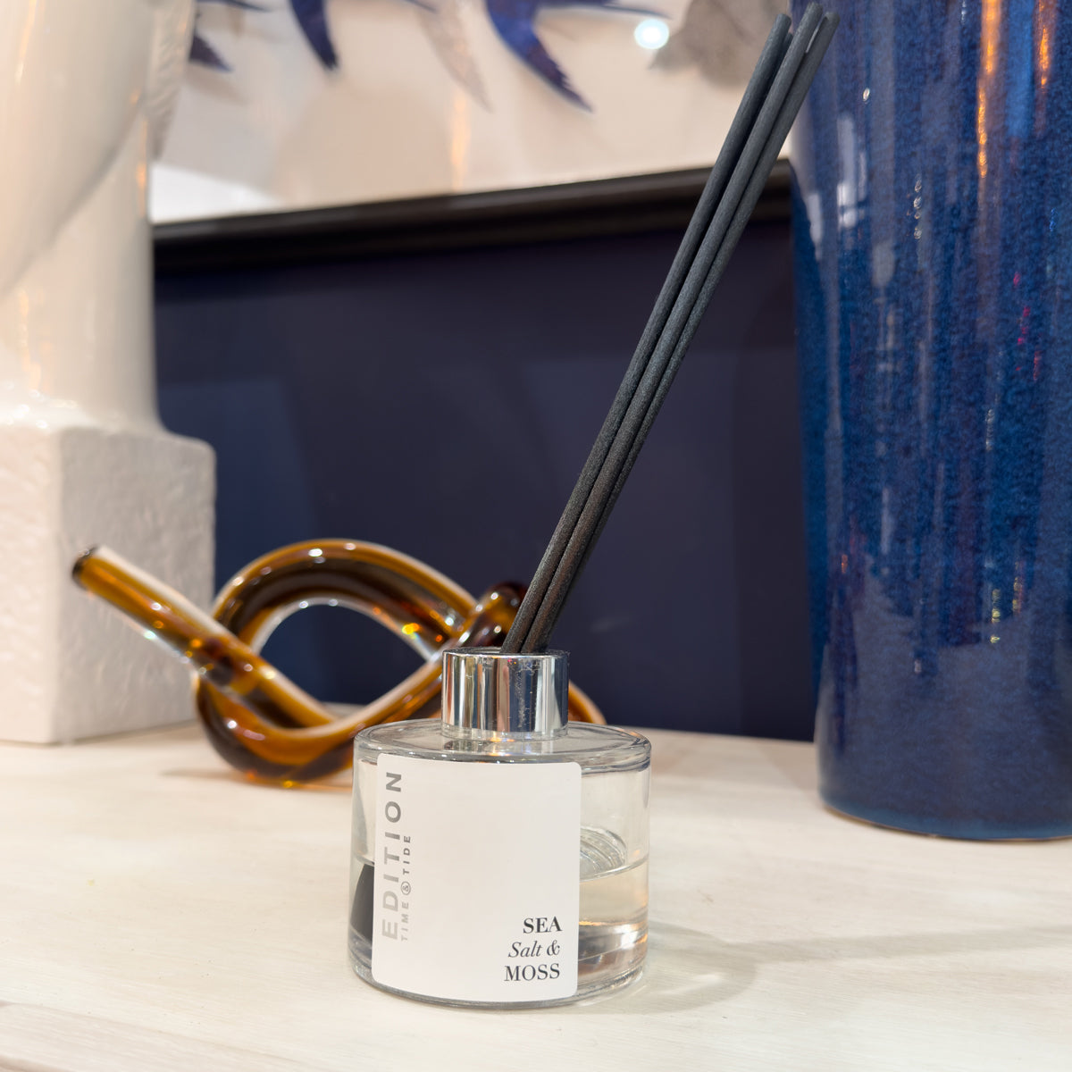 Luxury fragrance diffuser with black reeds on a surface with decorative items in the background