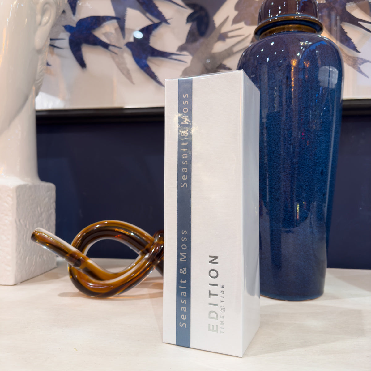 Decorative items including a blue ceramic urn, brown knot sculpture, and white box with 'Seasalt & Moss' branding on a shelf.