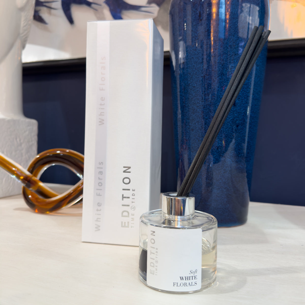 Diffuser bottle with black sticks and packaging on a white sideboard tabletop