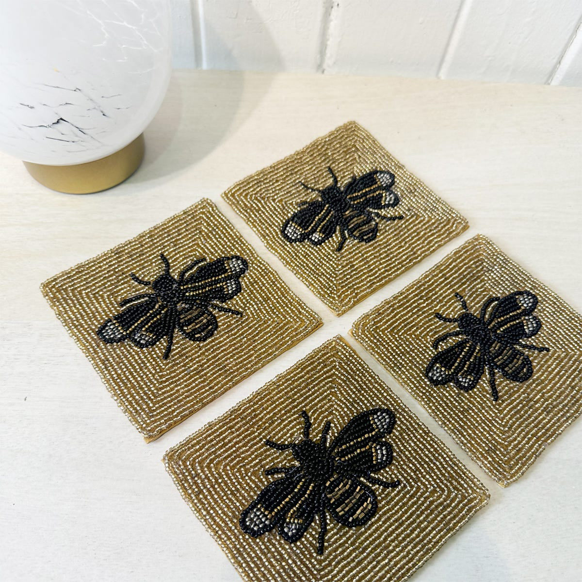 Four square beaded coasters with bee designs on a white surface.