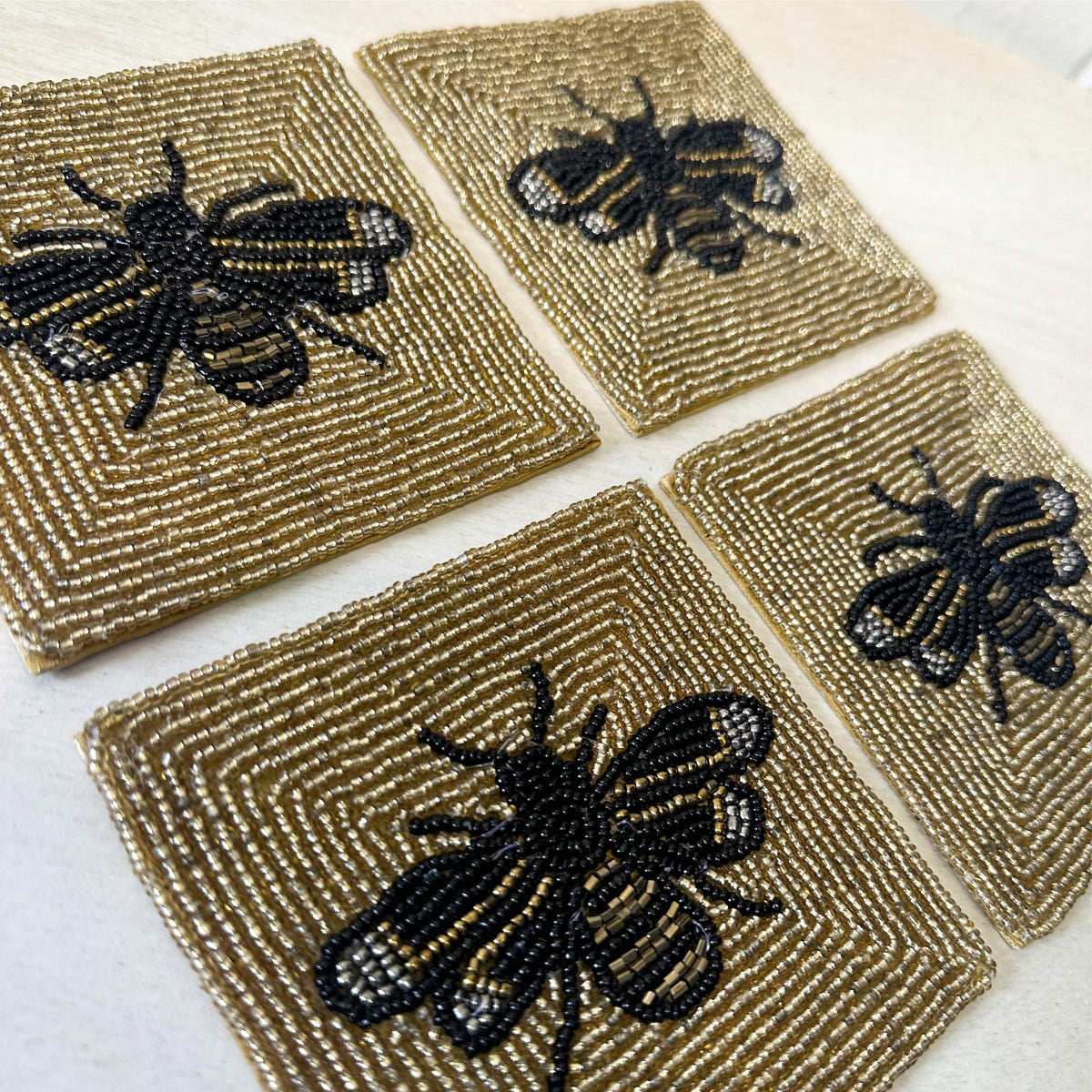 Four square coasters with black bee designs on a textured beige surface.