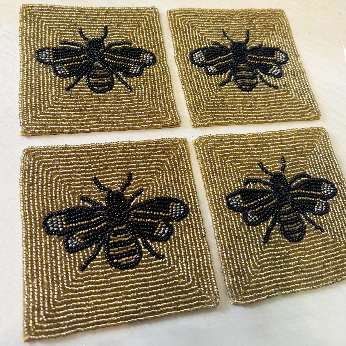 Four square coasters with bee designs on a textured surface